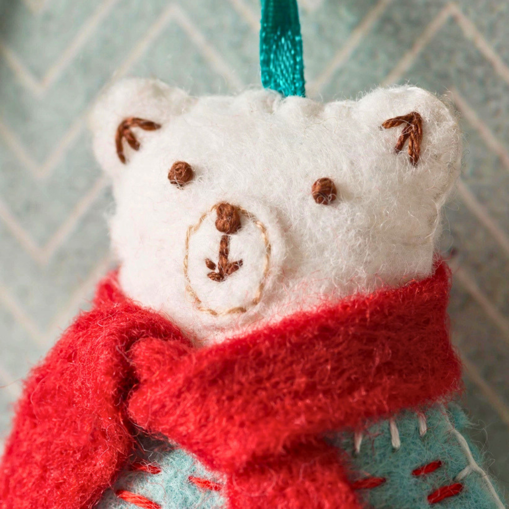 Close-up of the handmade polar bear showing its embroidered face, red scarf, ears and felt stitching.