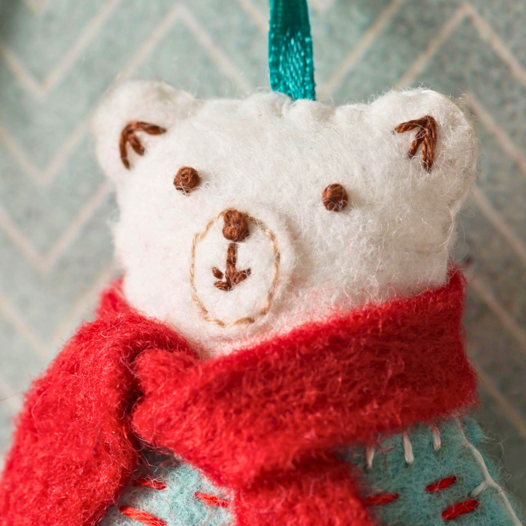 Close-up of the handmade polar bear showing its embroidered face, red scarf, ears and felt stitching.