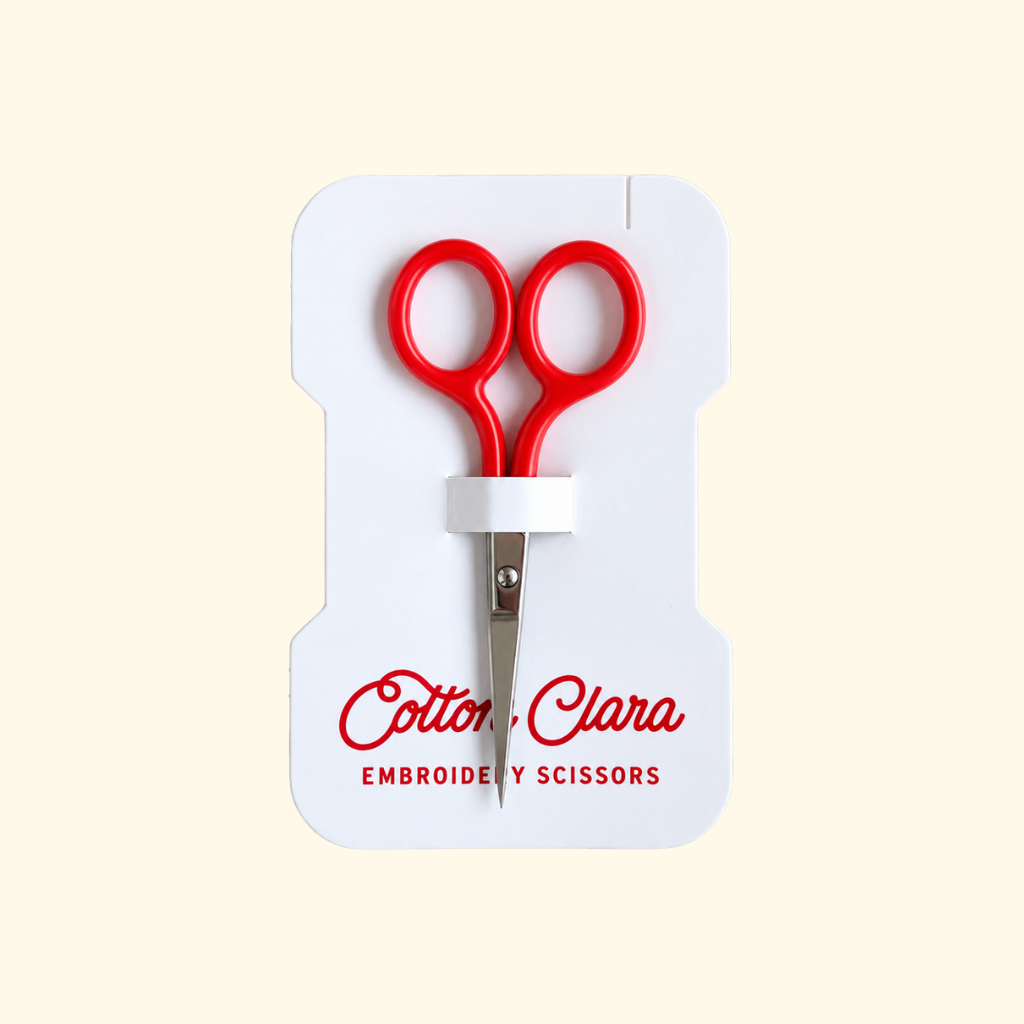 Poppy red Cotton Clara embroidery scissors with compact pointed blades, presented on branded product packaging.