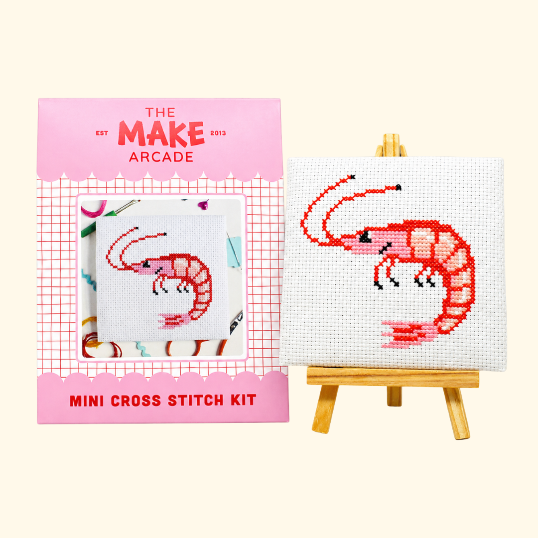 The Make Arcade Prawn Mini Cross Stitch Kit beside the completed design on a miniature easel.