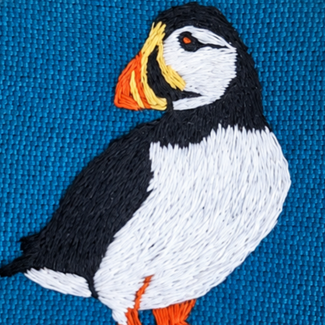 Close-up of the completed puffin mini embroidery design stitched on blue fabric.
