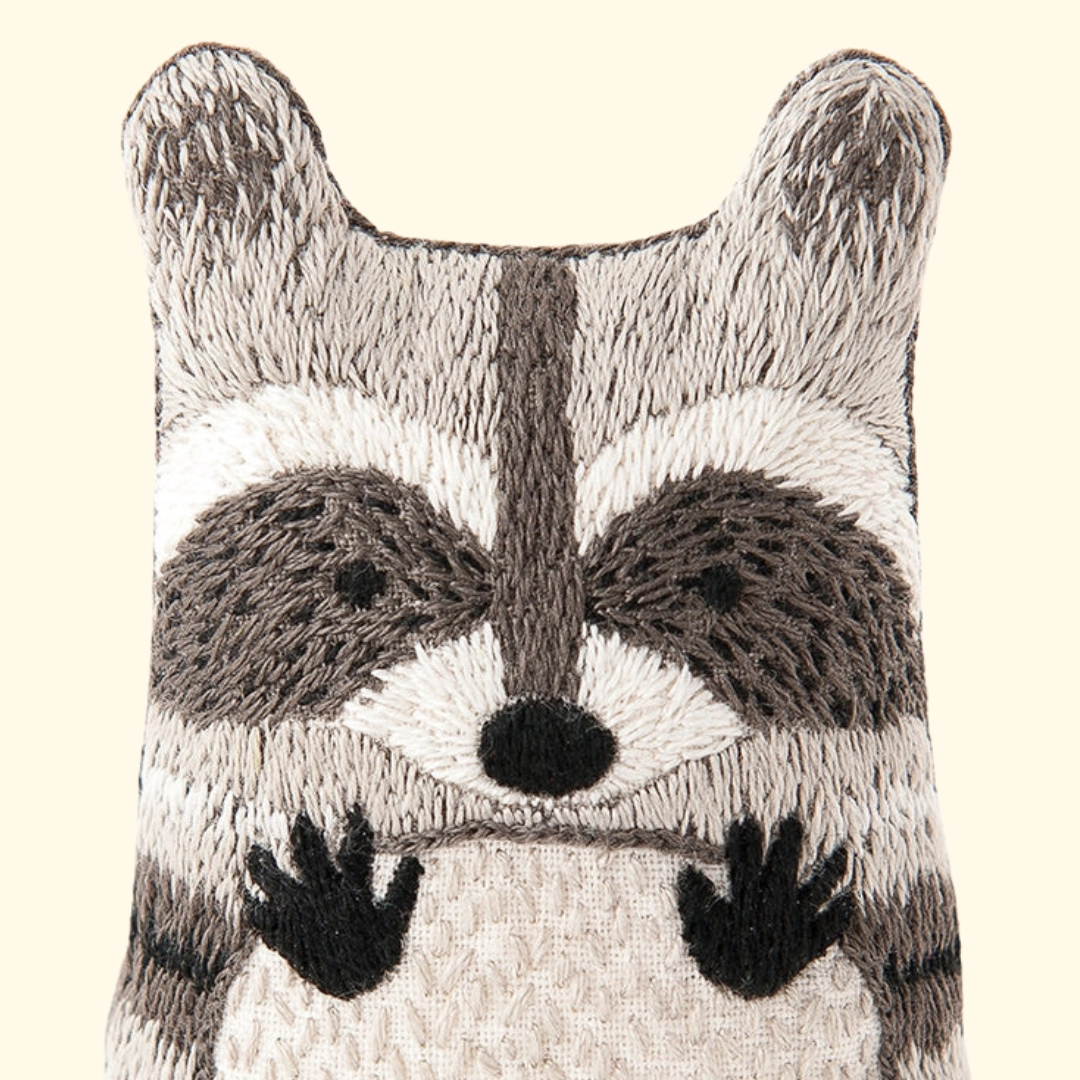 Close-up of the finished raccoon embroidery doll featuring a stitched mask, face and paws.