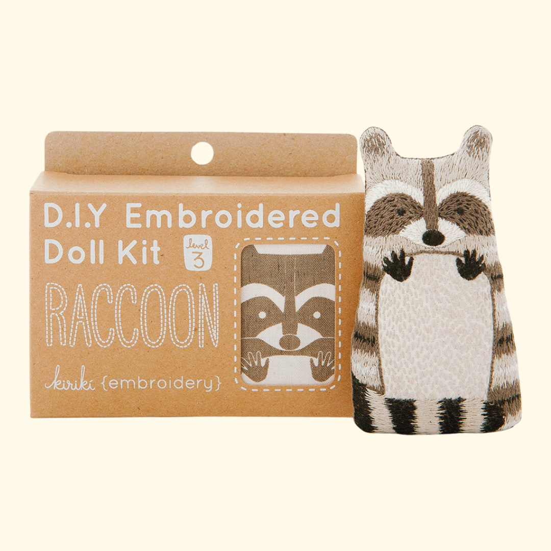Raccoon Embroidery Kit by Kiriki Press shown with the completed embroidered doll and packaging.