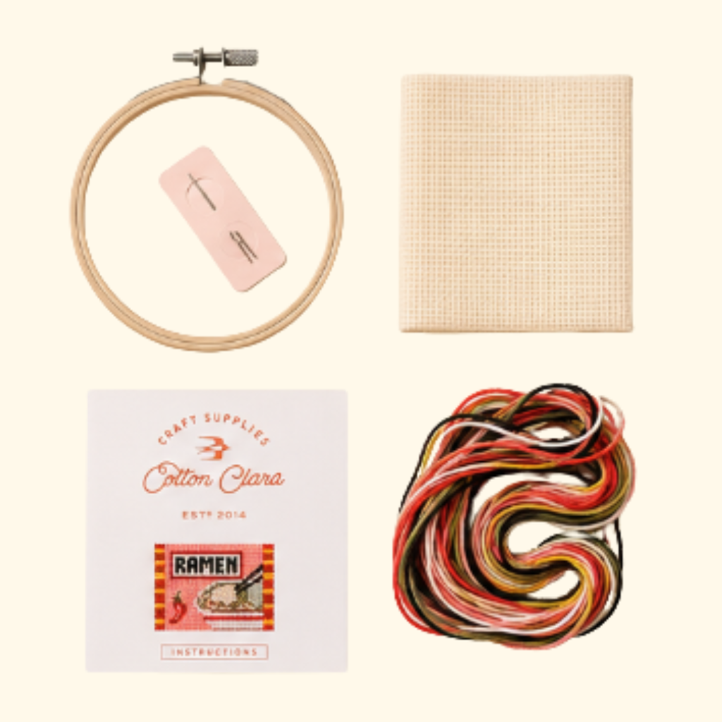 Contents of the Cotton Clara Ramen Cross Stitch Kit including hoop, Aida fabric, threads, needle and instructions.