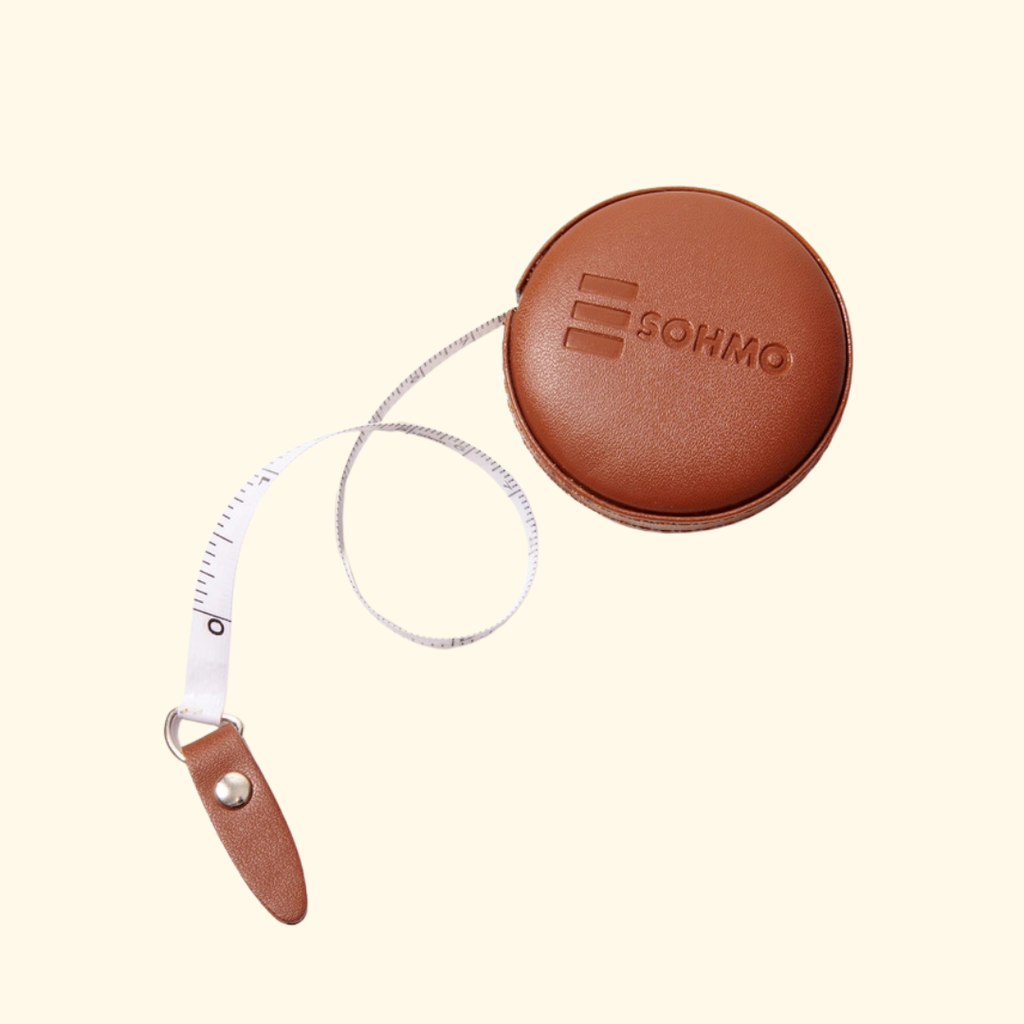 A brown leather retractable measuring tape with a circular case embossed with the brand name SOHMO, shown on a light cream background.
