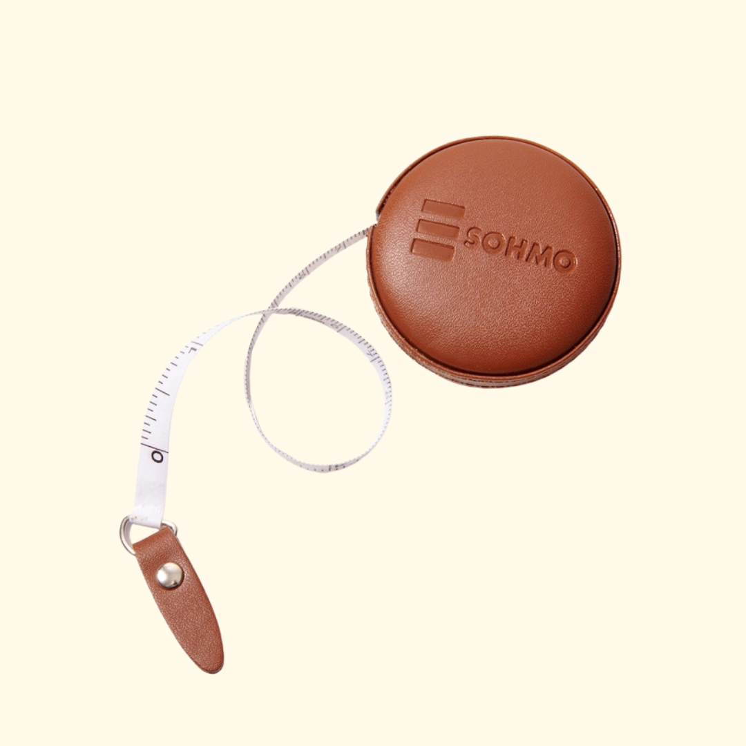 A brown leather retractable measuring tape with a circular case embossed with the brand name SOHMO, shown on a light cream background.
