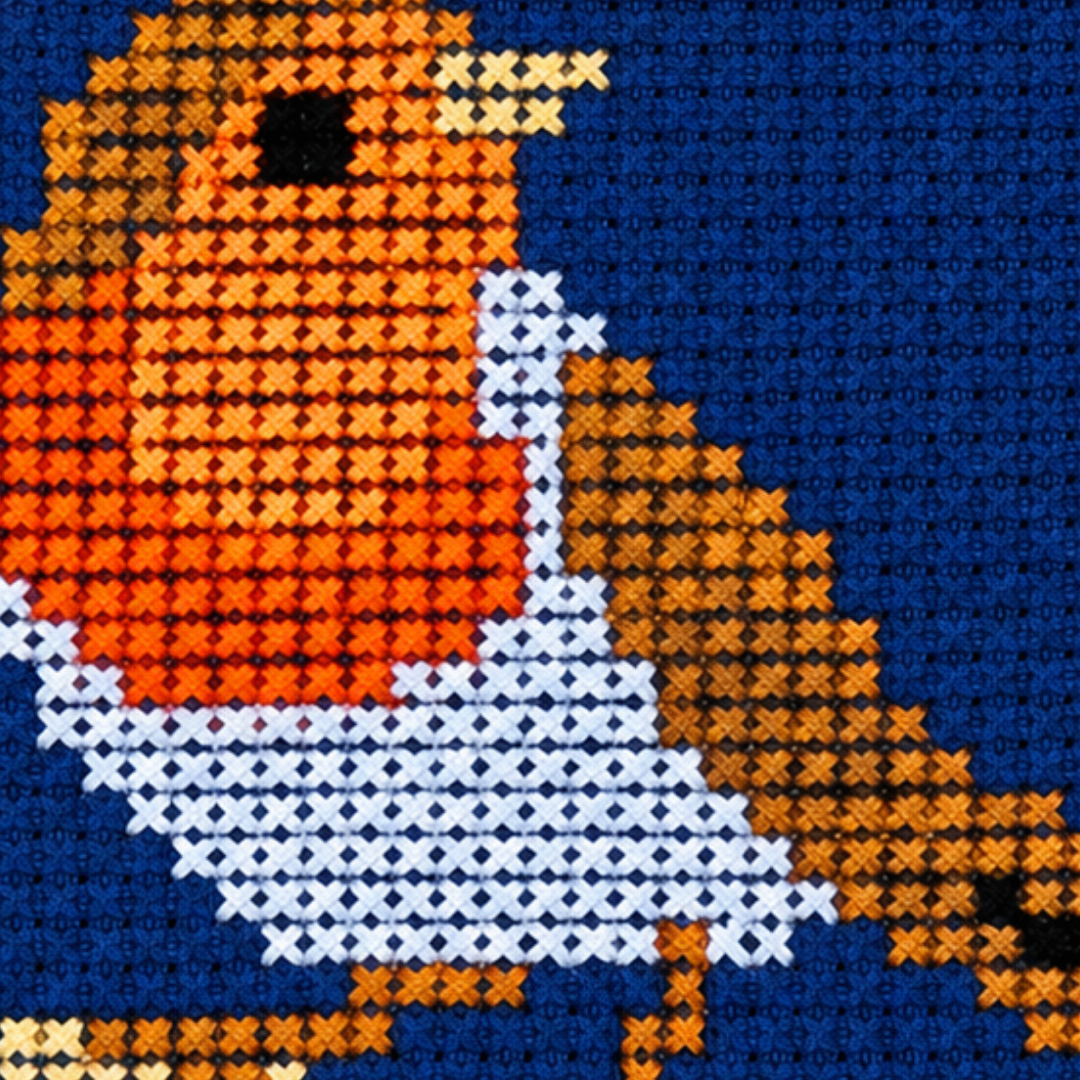 Close-up of an orange-breasted robin cross stitch design perched against a deep blue background.
