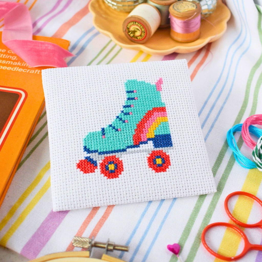 Finished Roller Derby Mini Cross Stitch Kit displayed with embroidery scissors, thread and colourful craft supplies.