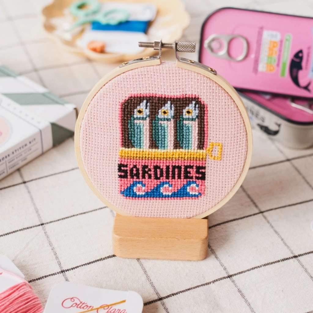 Finished sardines cross stitch displayed in a bamboo embroidery hoop on a wooden stand.