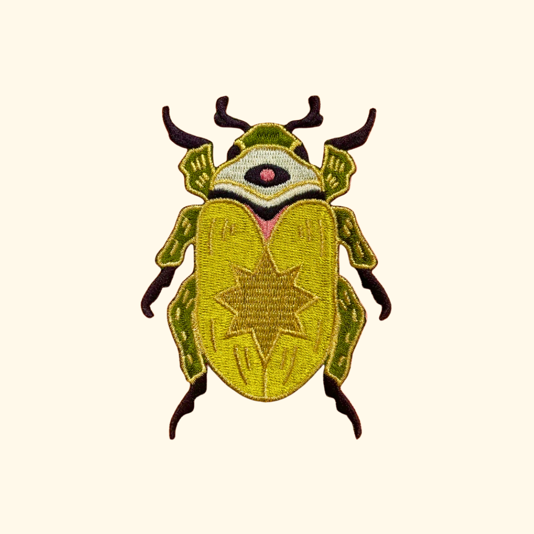 Green and yellow scarab beetle embroidered iron on patch by Ashlea Bechaz Illustration featuring detailed black legs and antennae on a cream background.