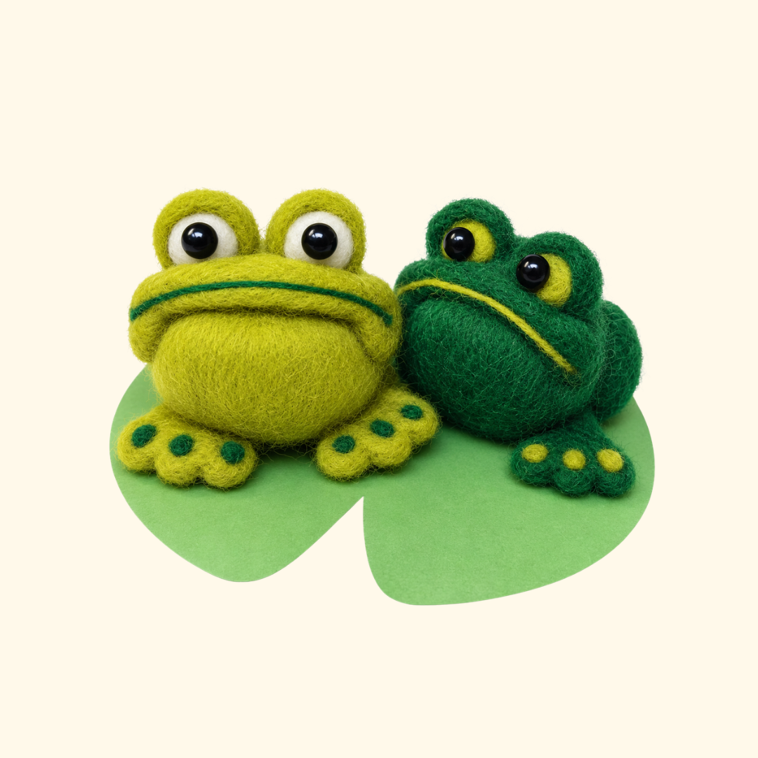 Two handmade green wool frogs in light and dark green, featuring raised eyes, smiling faces and little webbed feet, created using the Bergin And Bath needle felting kit.