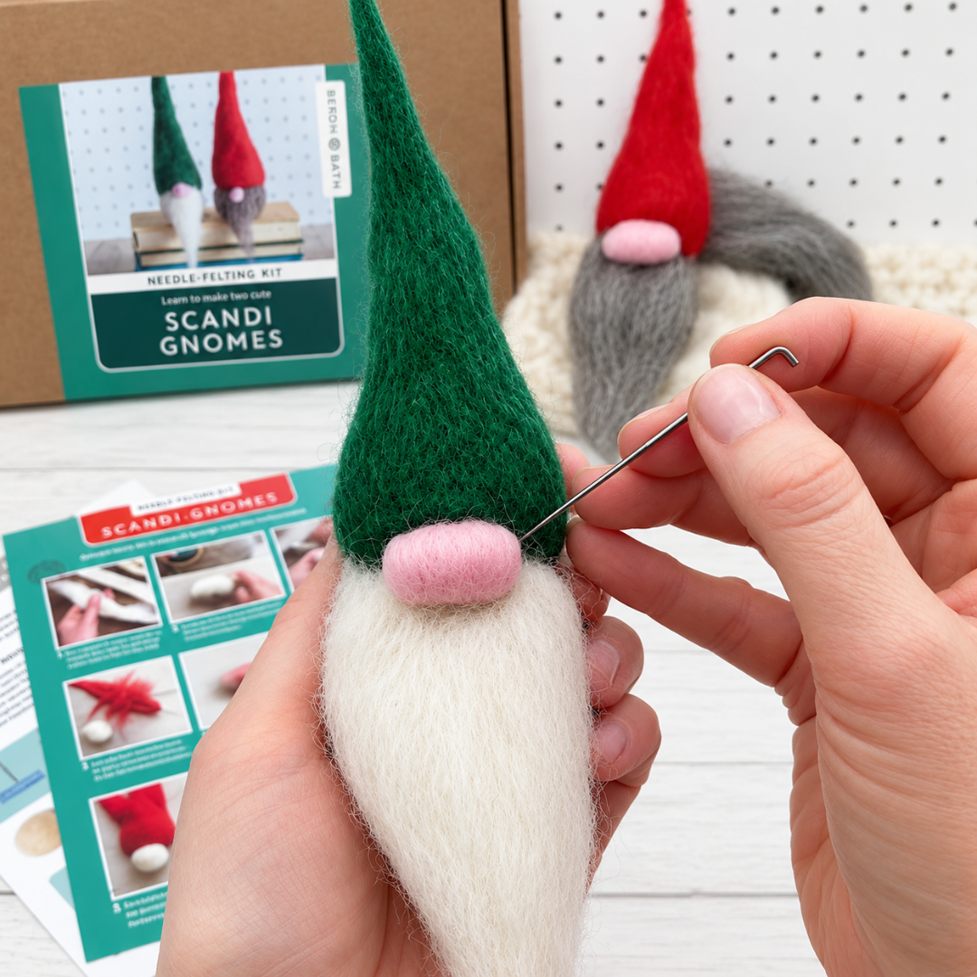 Close-up of hands holding a handmade Scandinavian gnome with a green pointed hat and white wool beard, demonstrating the needle felting process.