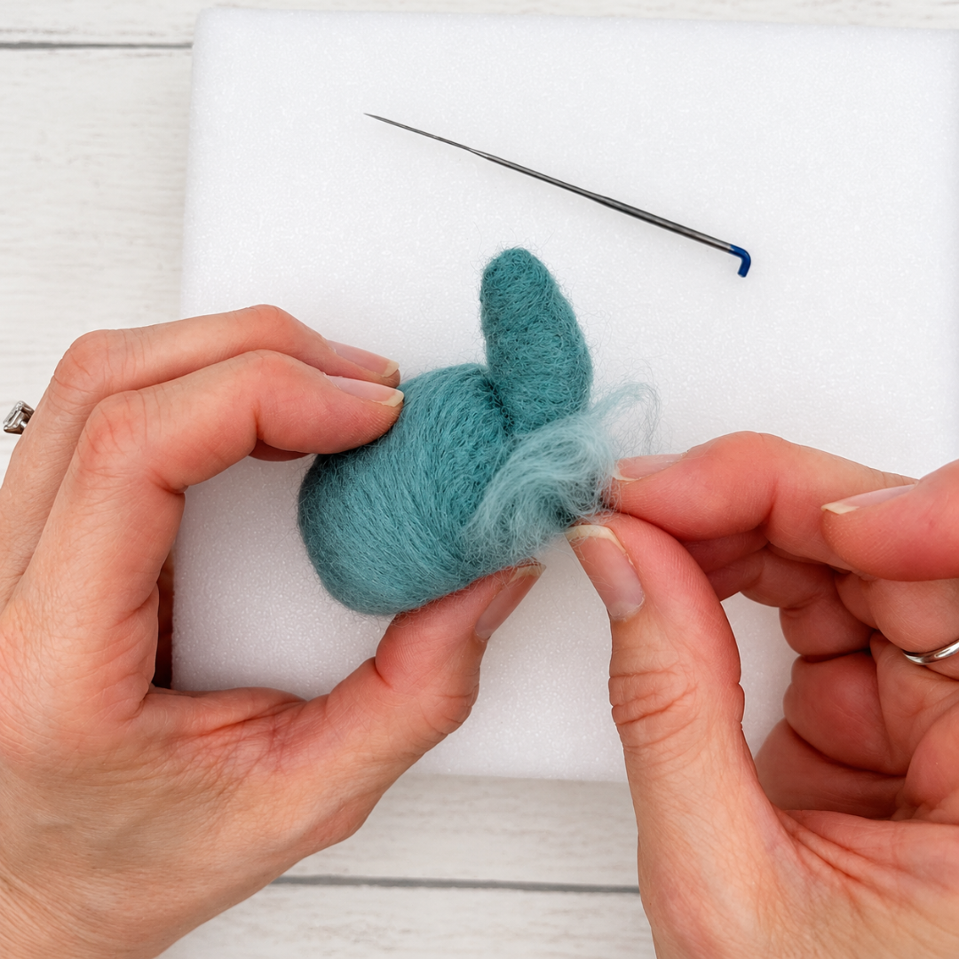 Hands shaping a blue wool whale using a felting needle, demonstrating the crafting process for the Bergin And Bath Set Of 2 Whales Needle Felting Kit.
