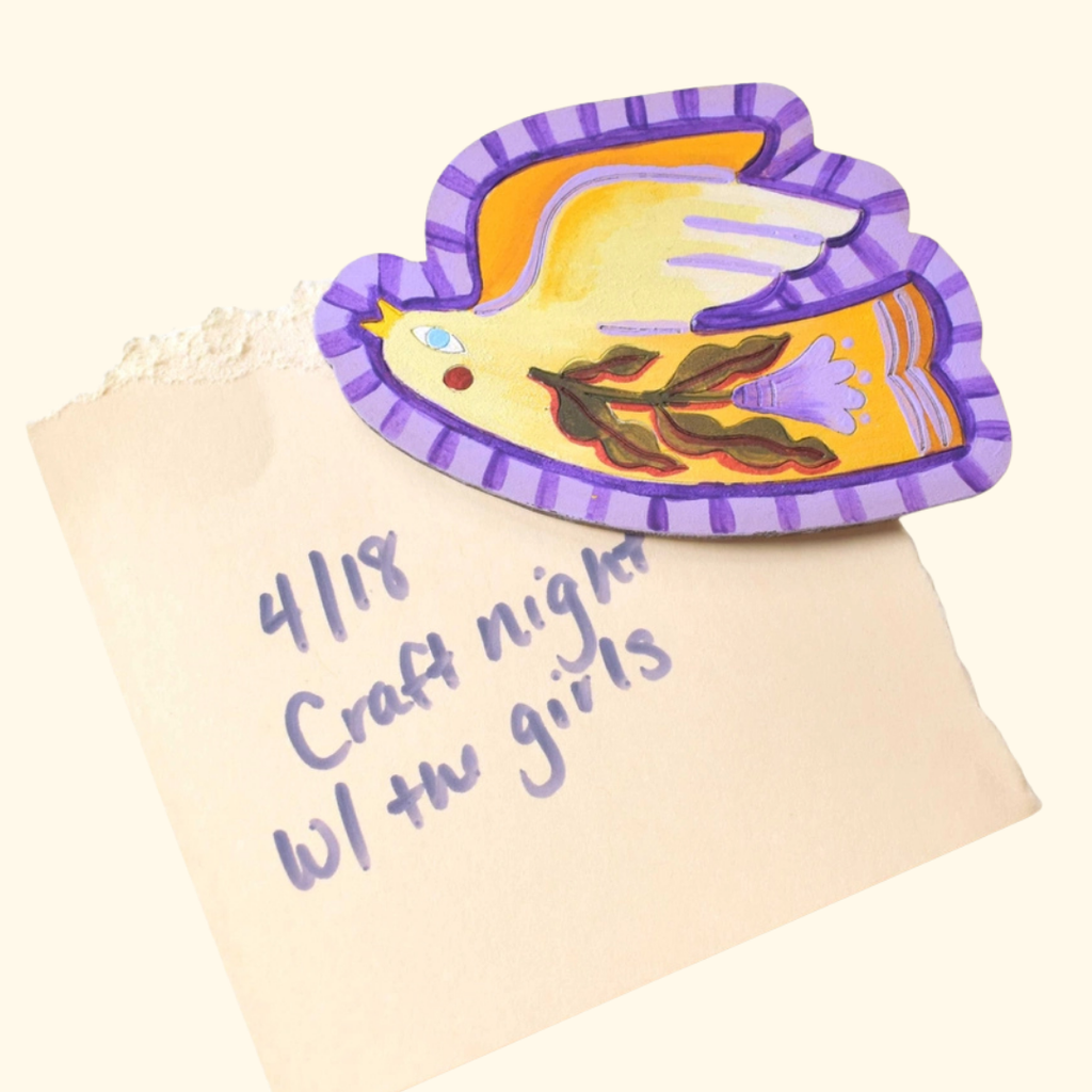 Folk bird wooden magnet being decorated with purple and yellow acrylic paint.