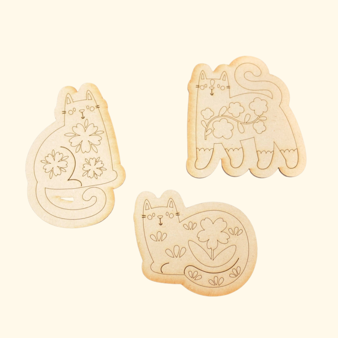 Three unpainted laser-cut wooden folk cats from the paint-your-own magnets kit.