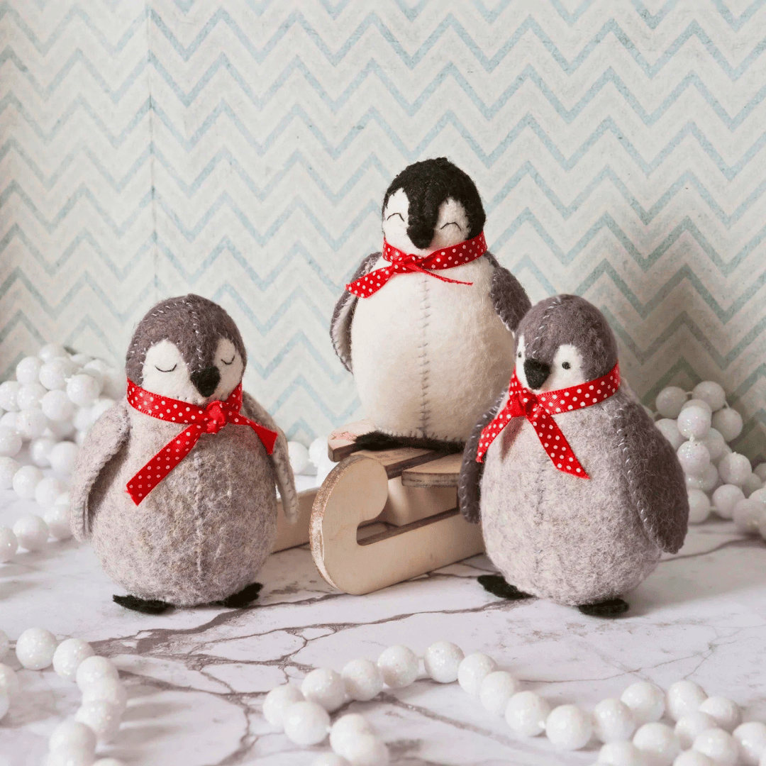 Finished felt penguins displayed together on a festive winter scene with decorative accessories.