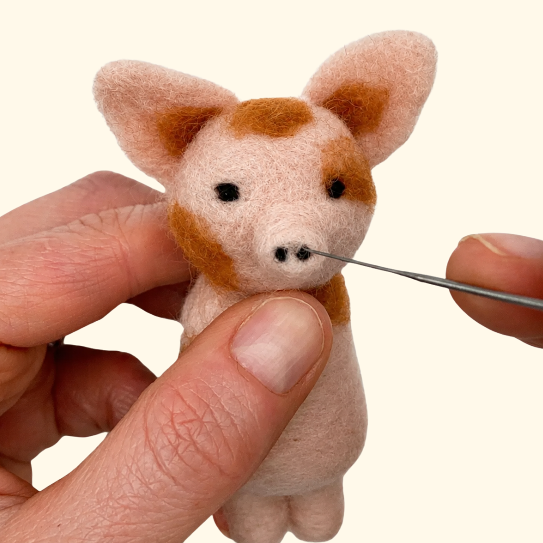 Needle felting the face of a small pink pig decoration by hand