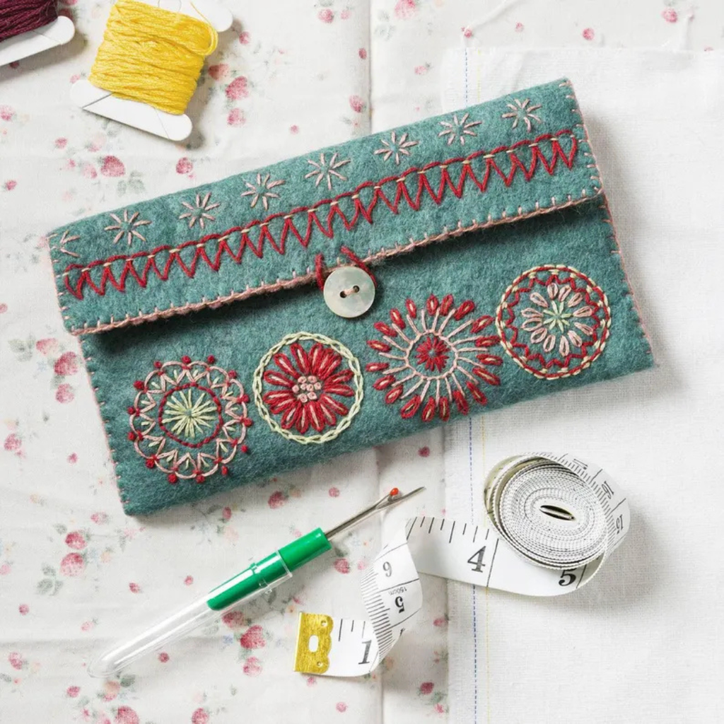 Finished embroidered sewing pouch displayed with measuring tape, thread and sewing accessories