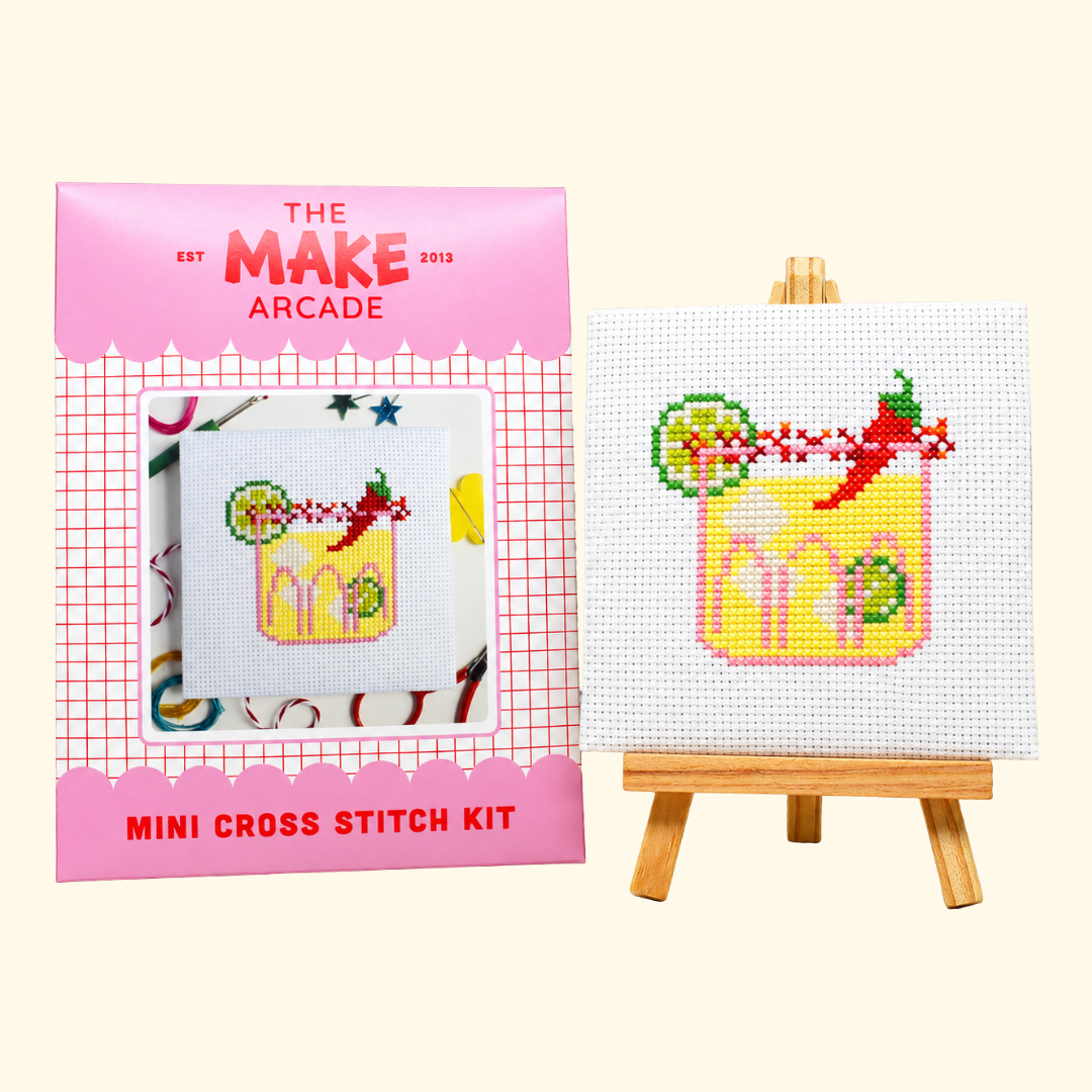 The Make Arcade Spicy Marg Mini Cross Stitch Kit beside the completed design on a miniature easel.