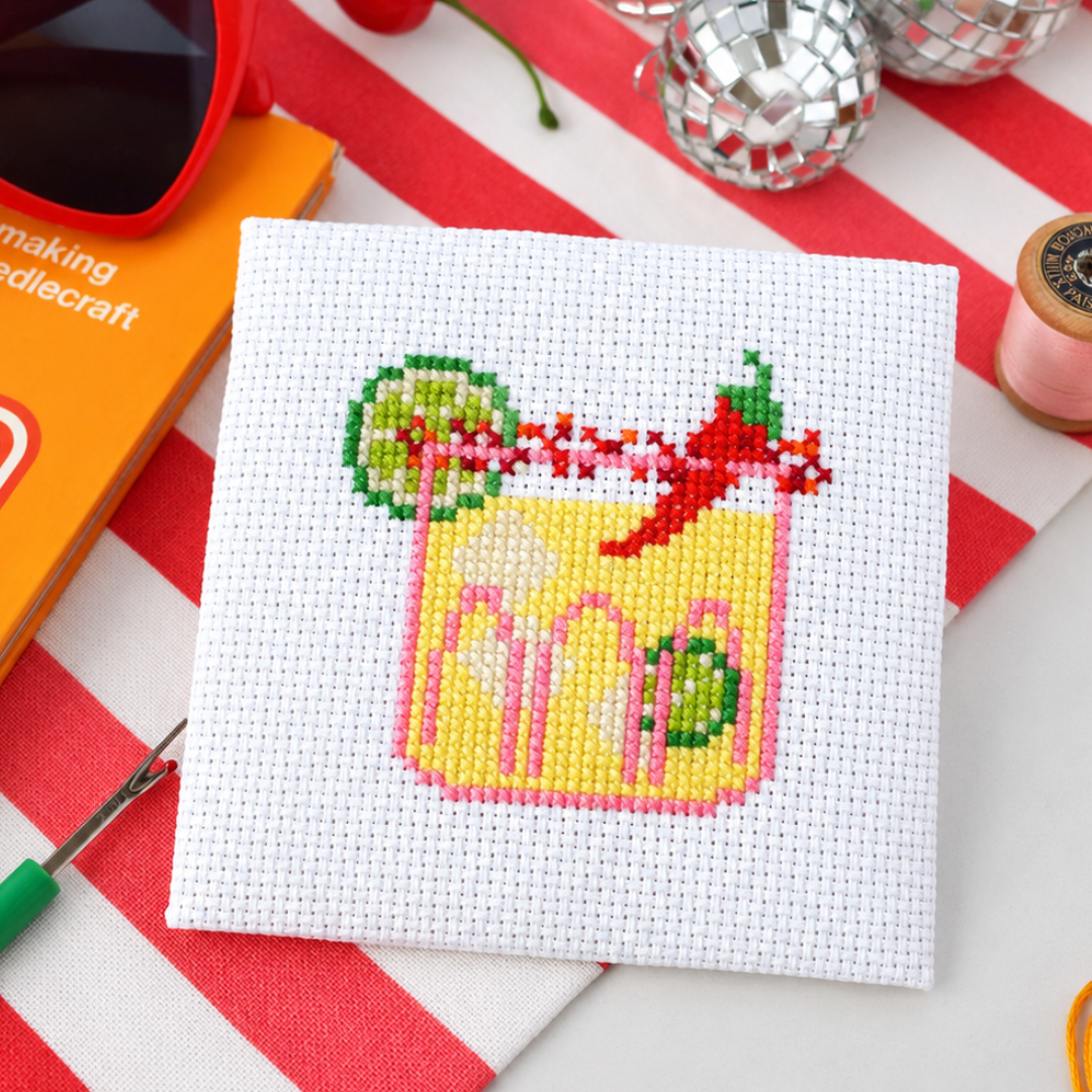 Spicy margarita cross stitch design surrounded by scissors, thread, stars and a yellow flower.