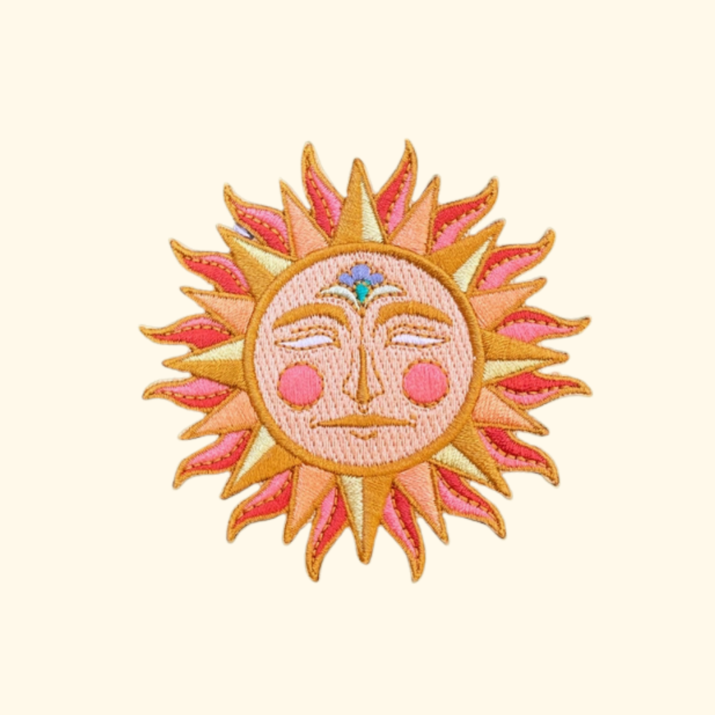 Colourful embroidered sun iron on patch by Ashlea Bechaz Illustration featuring a smiling face, pink and yellow details and orange sun rays on a cream background.