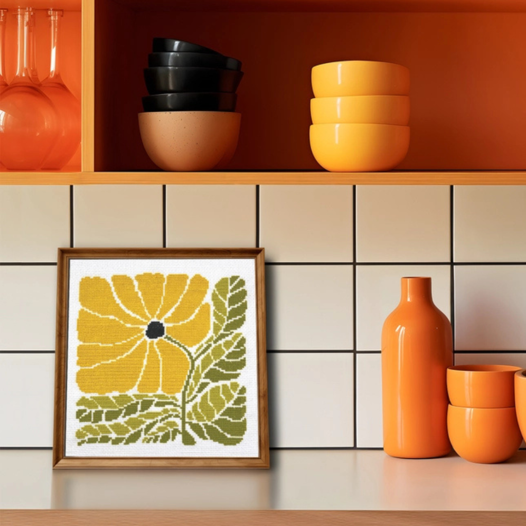 Framed Sunny Blossom Grid cross stitch displayed on a shelf with modern home décor in warm tones.