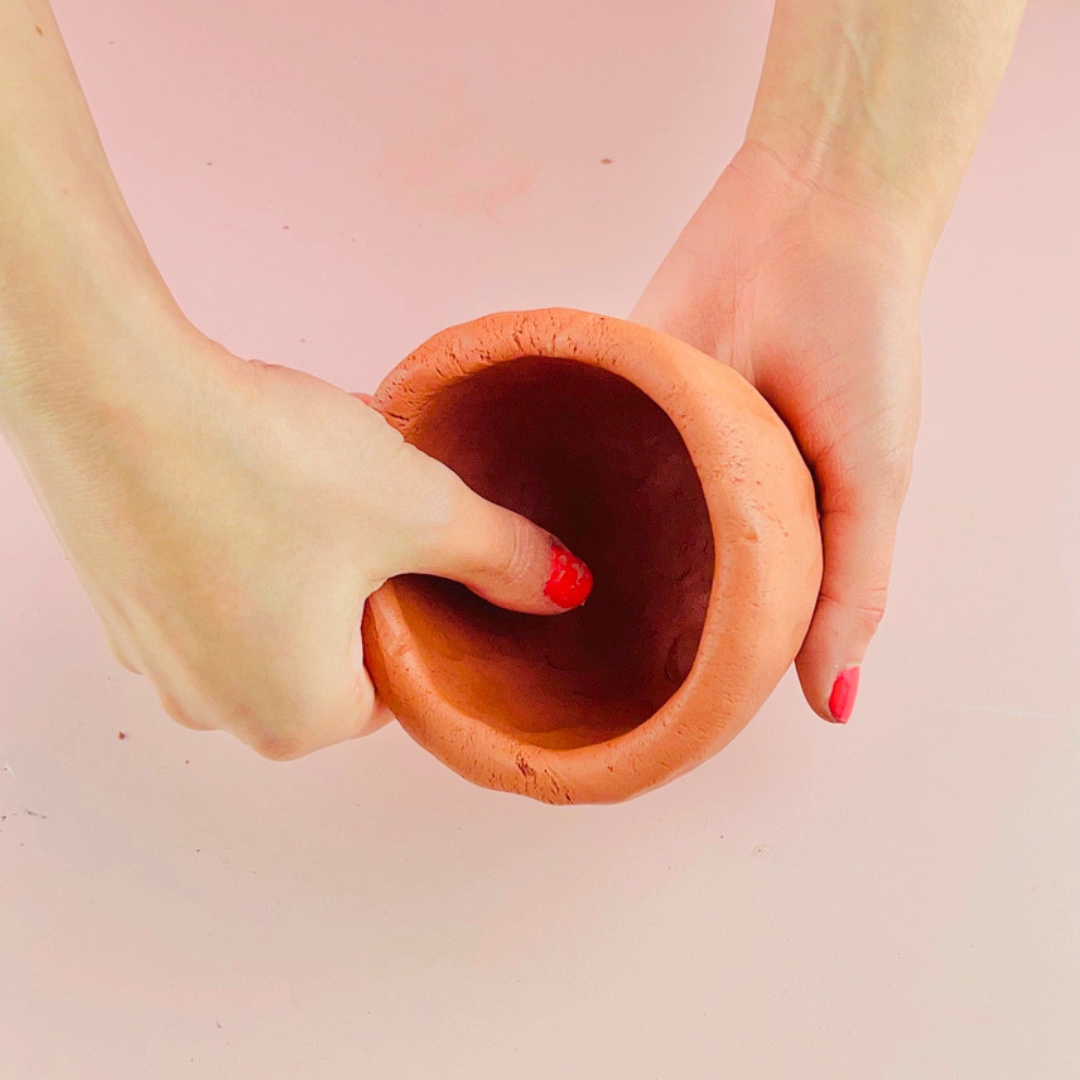 Hands shaping terracotta clay using the pinch pot technique to create a handmade planter.