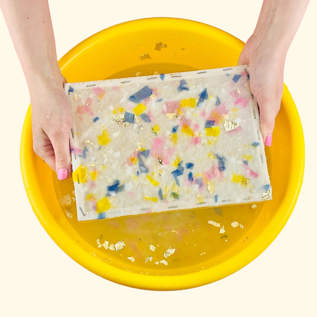 Freshly made terrazzo-style handmade paper sheet lifted from a yellow tray during the papermaking process.