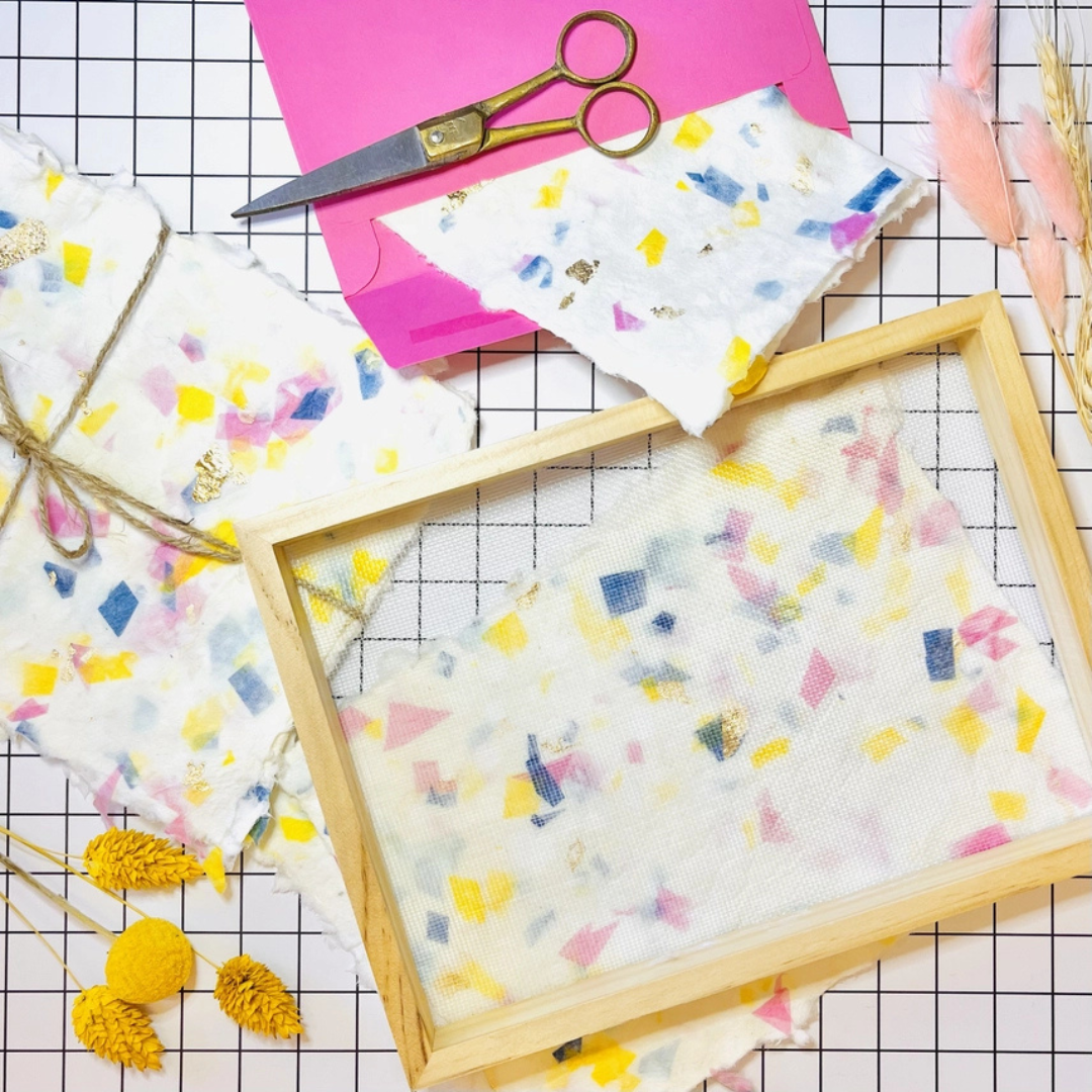 Handmade terrazzo paper drying in a wooden mould and deckle surrounded by colourful paper making materials.