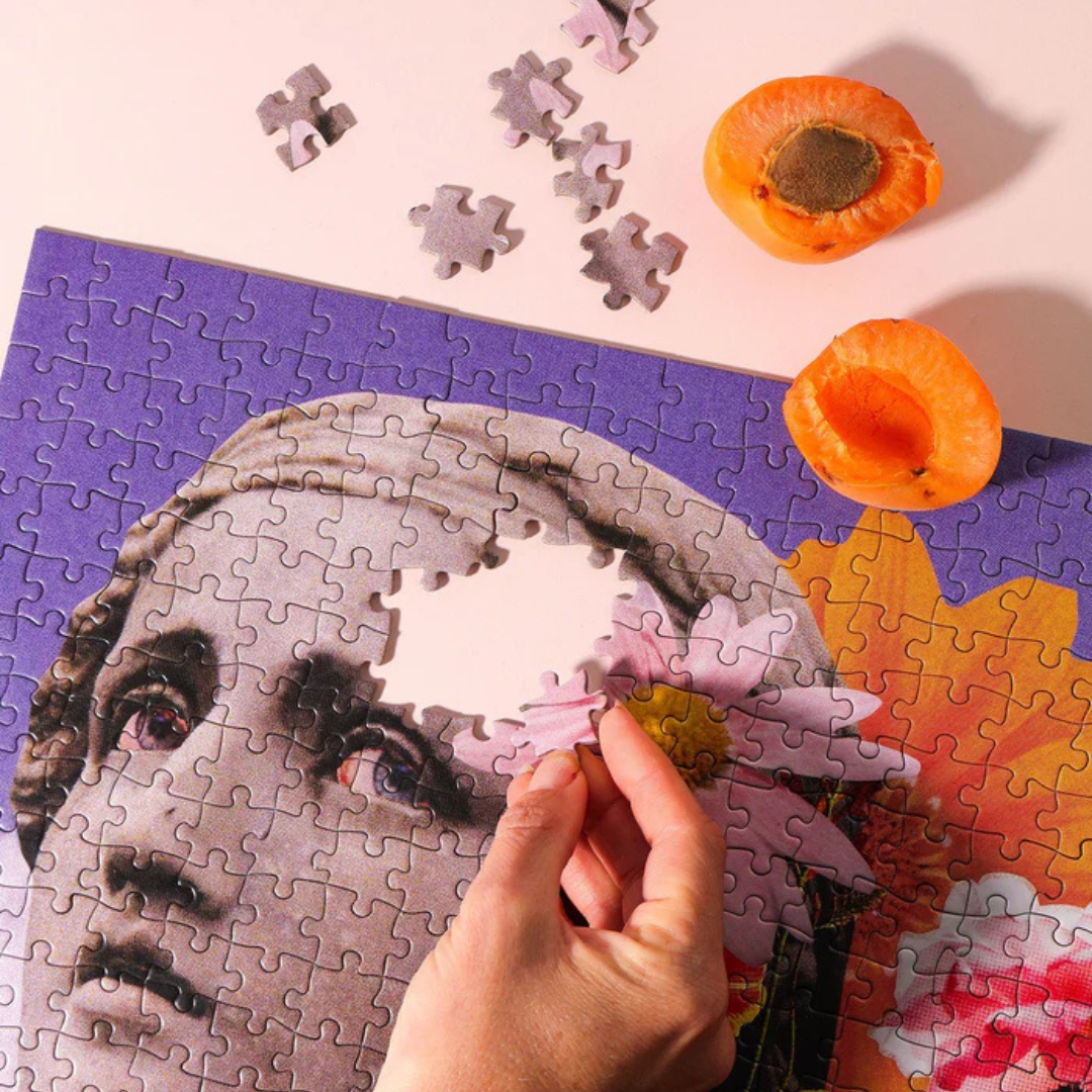 Close up detail of The Lovers puzzle with hand placing a puzzle piece beside floral collage artwork.
