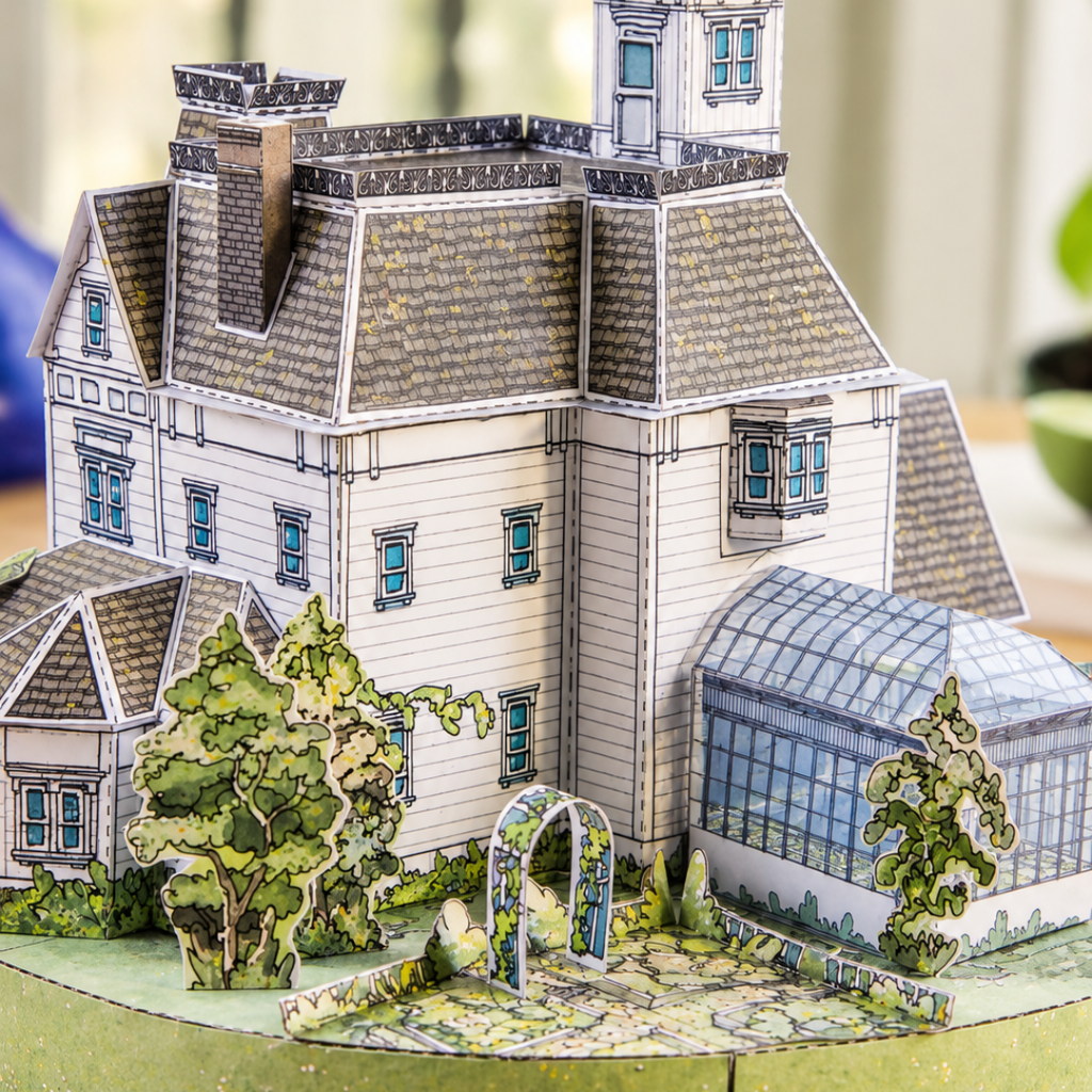 Close-up of the completed Owens House paper model showing detailed windows, textured roof tiles, Victorian architectural features and miniature garden landscaping.