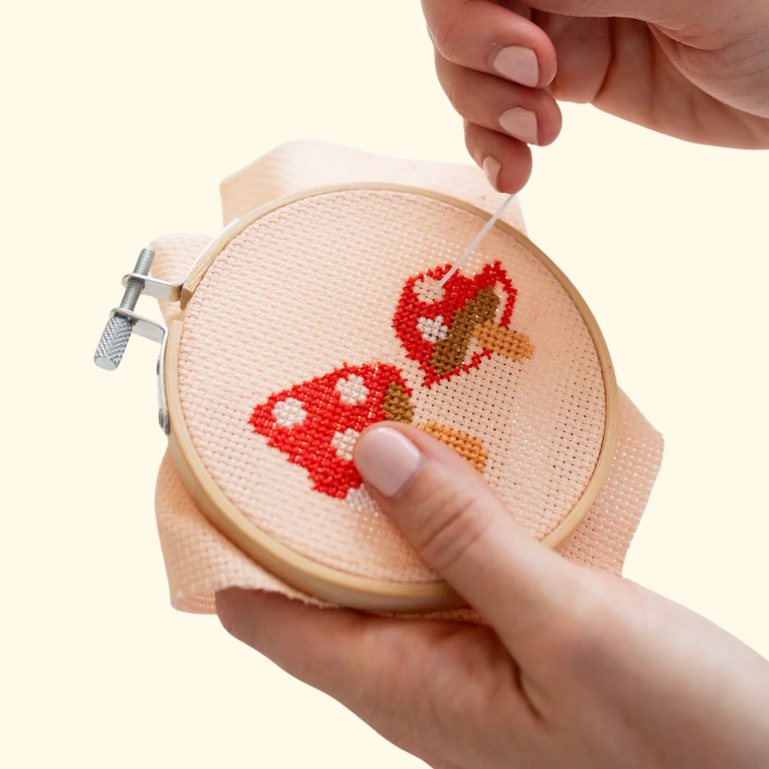 Hands stitching the toadstools cross stitch design using the Cotton Clara craft kit.