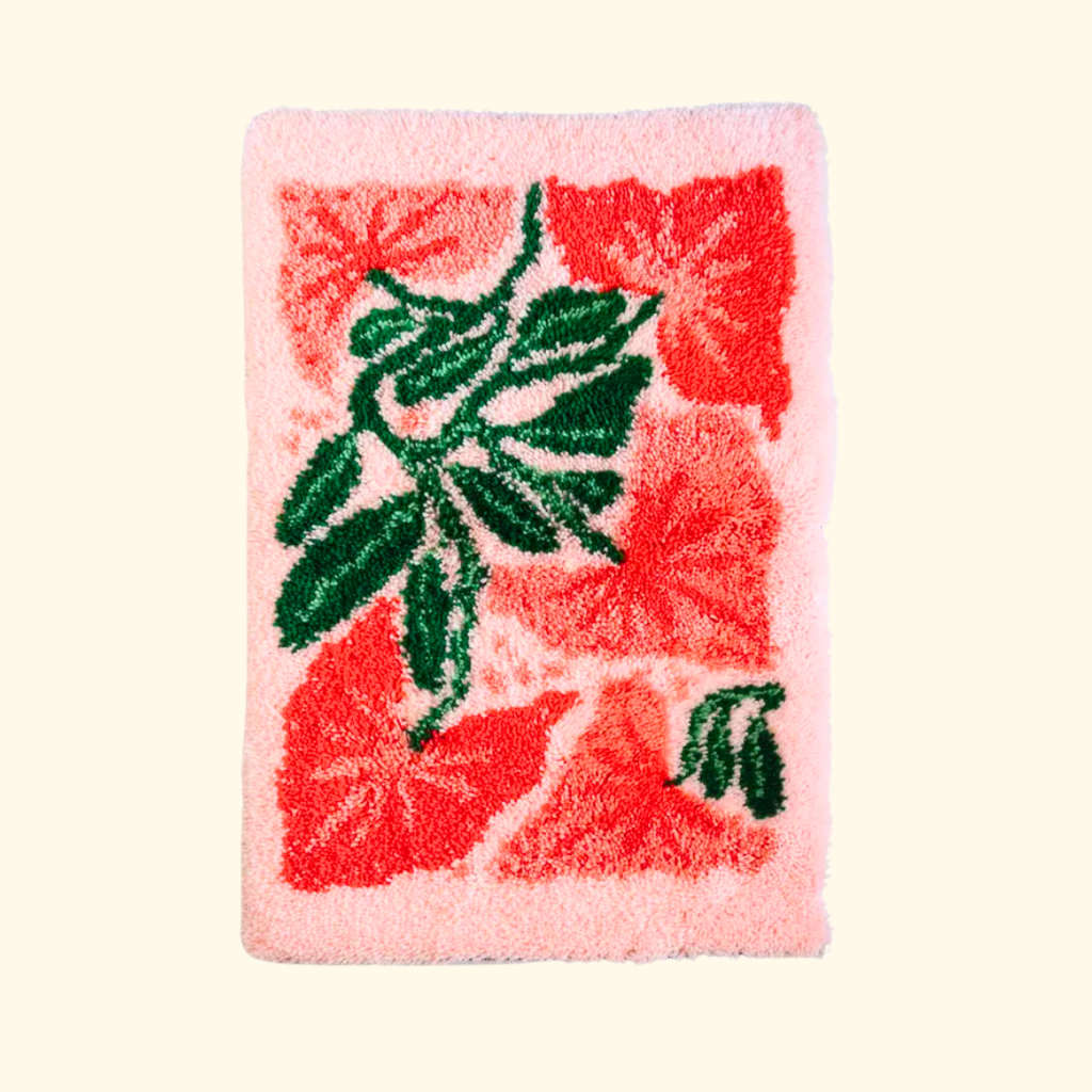 Finished latch hook rug featuring tropical leaves on a coral pink background, created with a latch hook kit for beginners.