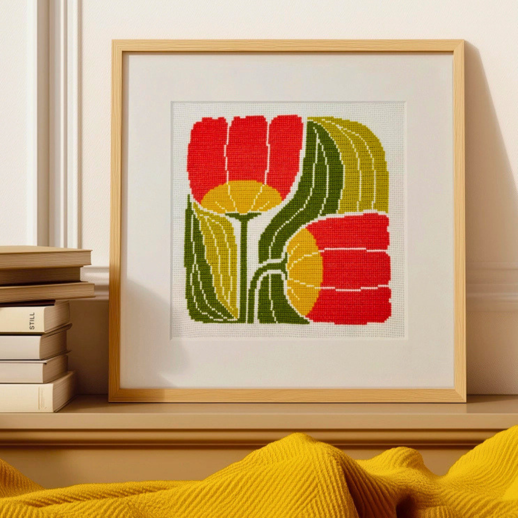 Framed Twin Blooms Grid cross stitch design by Budgiegoods displayed on a shelf with books and home decor.