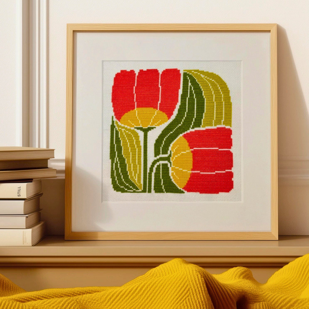 Framed Twin Blooms Grid cross stitch design by Budgiegoods displayed on a shelf with books and home decor.