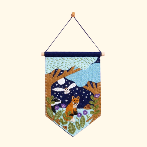 Felt woodland wall hanging featuring a fox, owl, moonlit sky and forest scene hanging from a wooden dowel