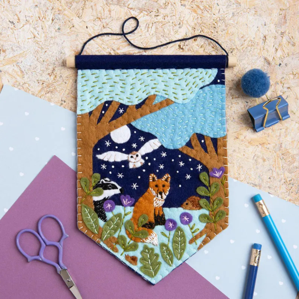 Completed woodland felt wall hanging displayed with craft supplies and felt pom poms